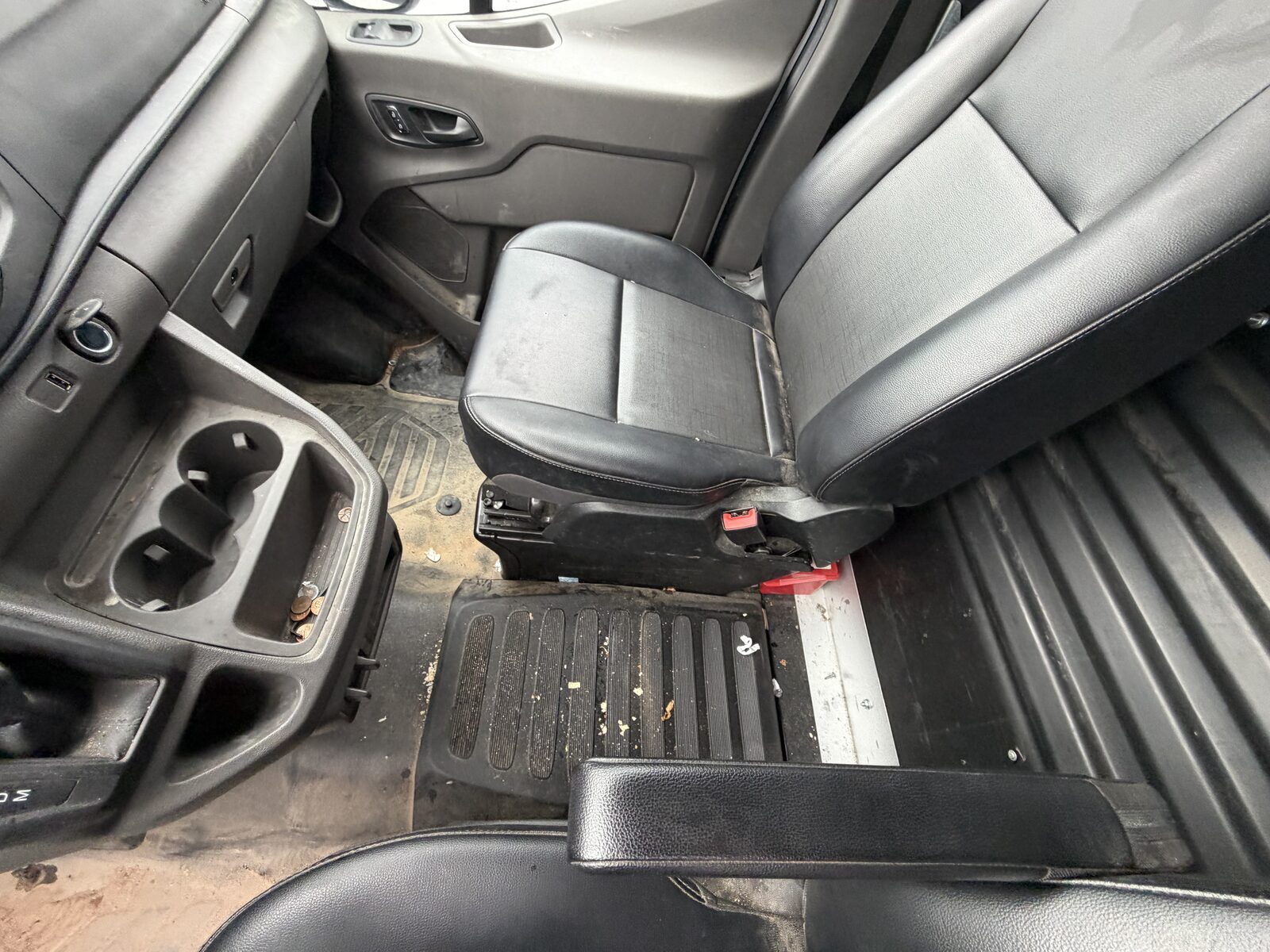 Van interior before detailing: dirty rubber floor with debris, scuffed plastics, and grime around the seat base.