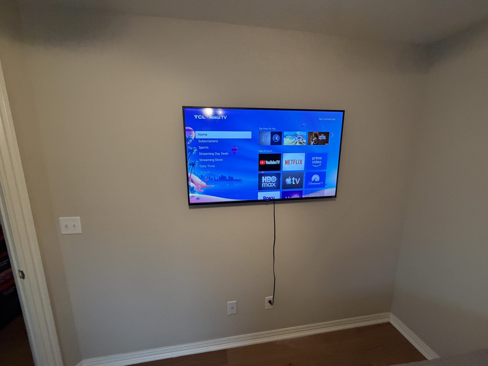 Wall-mounted TV with Roku interface in a blue-walled room